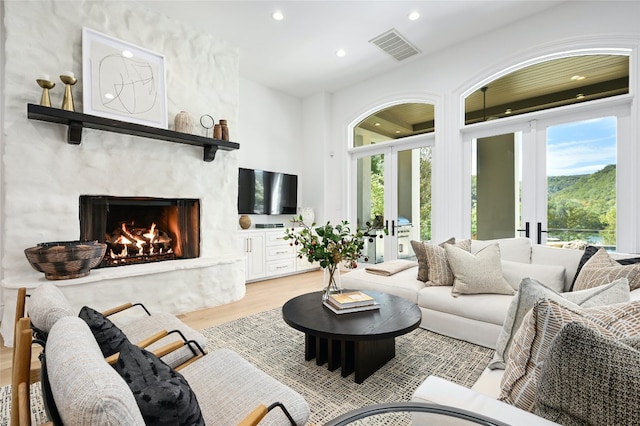 living area with visible vents, recessed lighting, french doors, light wood-style floors, and a premium fireplace