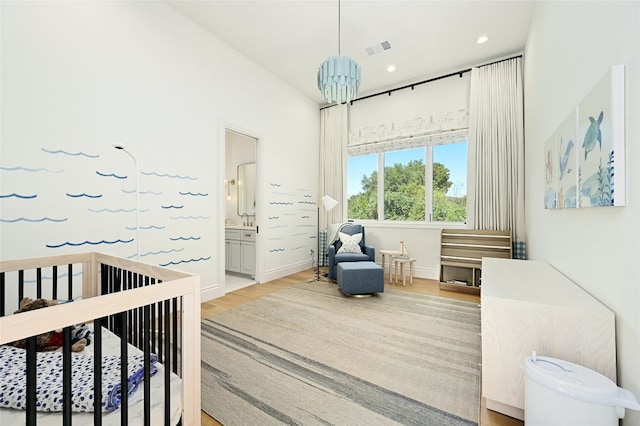 bedroom with ensuite bathroom, a crib, a chandelier, and light hardwood / wood-style flooring