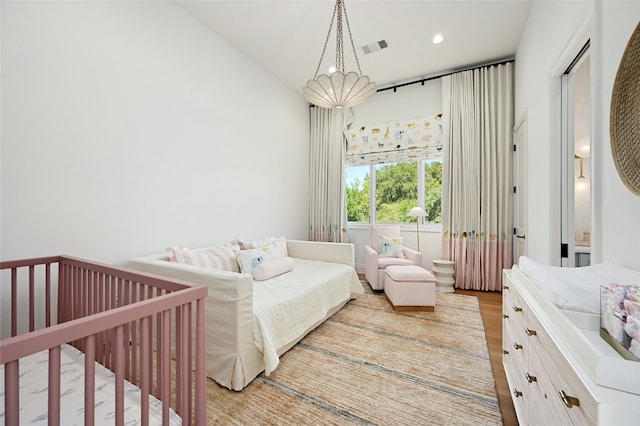 bedroom with lofted ceiling, light hardwood / wood-style flooring, and a crib