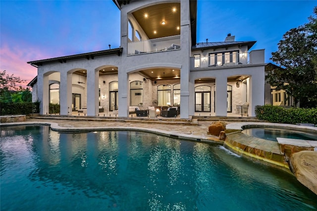 back house at dusk with a patio area, a balcony, and a pool with hot tub