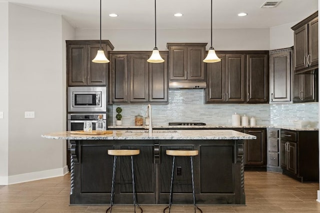 kitchen featuring appliances with stainless steel finishes, an island with sink, and light stone counters