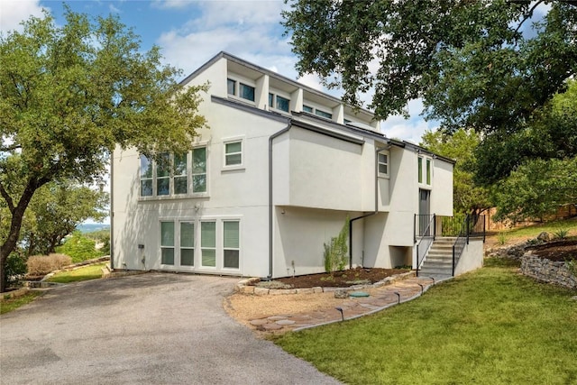 rear view of property with stucco siding, driveway, and a lawn