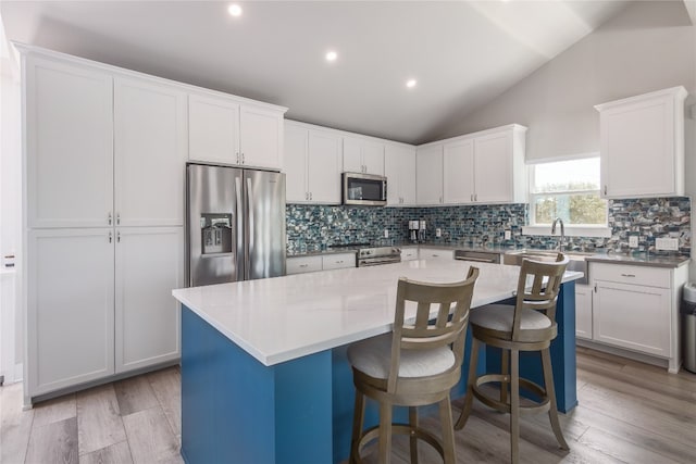 kitchen with light hardwood / wood-style flooring, a kitchen island, stainless steel appliances, and vaulted ceiling