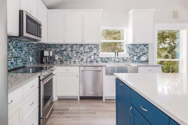 kitchen with blue cabinets, appliances with stainless steel finishes, sink, white cabinetry, and light wood-type flooring