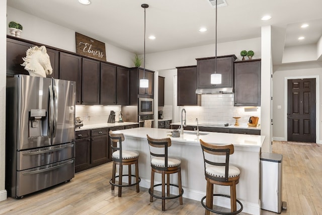 kitchen with stainless steel refrigerator with ice dispenser, a center island with sink, light hardwood / wood-style flooring, and decorative light fixtures