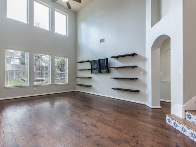 unfurnished living room with ceiling fan, dark hardwood / wood-style floors, and a towering ceiling