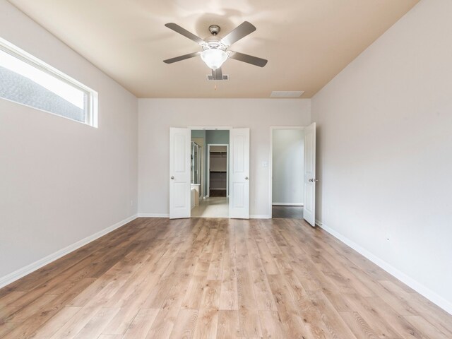 unfurnished bedroom with light hardwood / wood-style flooring, ceiling fan, and a walk in closet