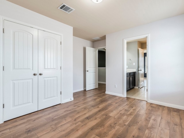 unfurnished bedroom featuring light wood-type flooring, ensuite bath, and a closet