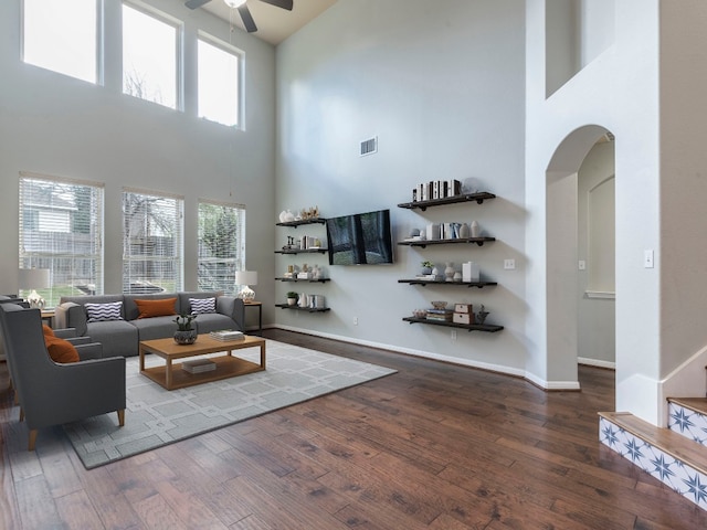 living room with dark wood-type flooring, ceiling fan, and a high ceiling