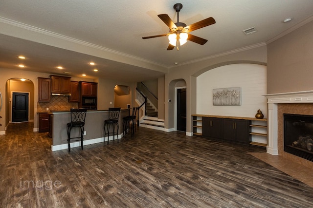 living room with dark wood-type flooring, ceiling fan, ornamental molding, a textured ceiling, and a tiled fireplace