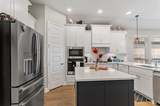 kitchen featuring light wood-type flooring, pendant lighting, white cabinetry, stainless steel appliances, and sink