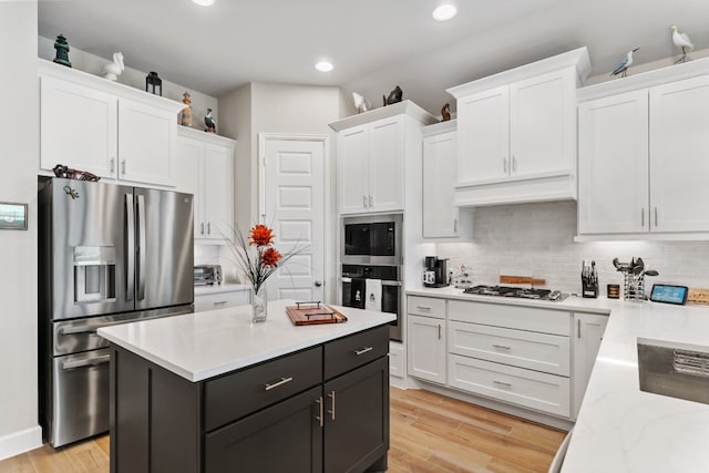 kitchen featuring light wood-type flooring, white cabinetry, stainless steel appliances, a center island, and decorative backsplash