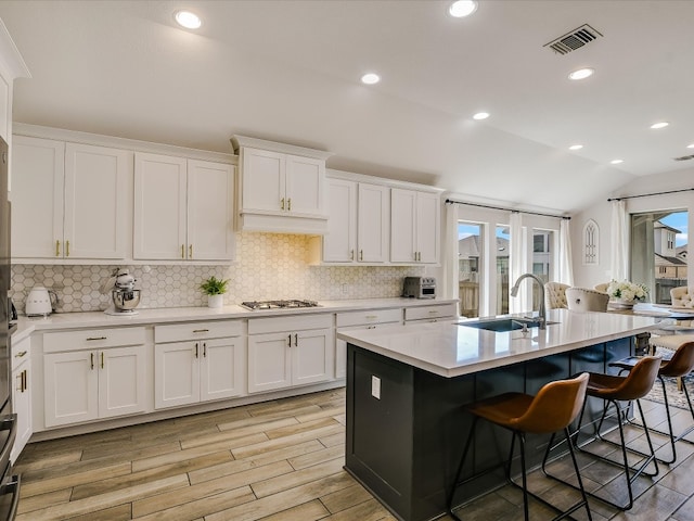 kitchen with white cabinetry, light hardwood / wood-style flooring, an island with sink, decorative backsplash, and lofted ceiling