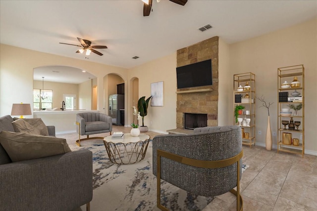 tiled living room with ceiling fan with notable chandelier and a fireplace