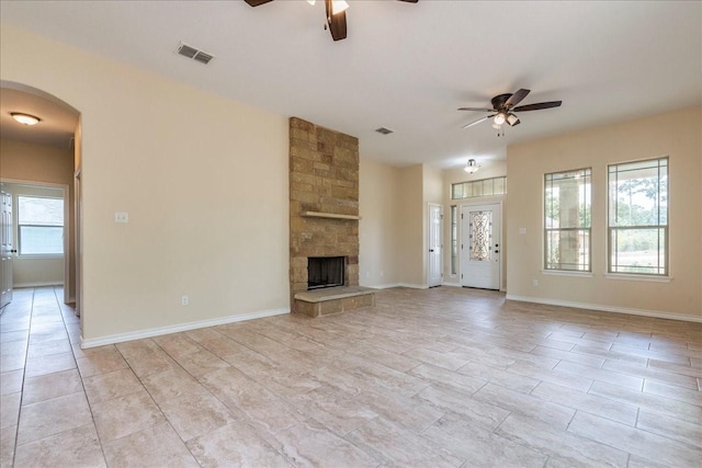 unfurnished living room with ceiling fan, a healthy amount of sunlight, and a stone fireplace