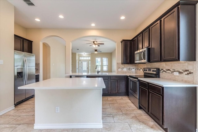 kitchen featuring stainless steel appliances, kitchen peninsula, ceiling fan, sink, and tasteful backsplash