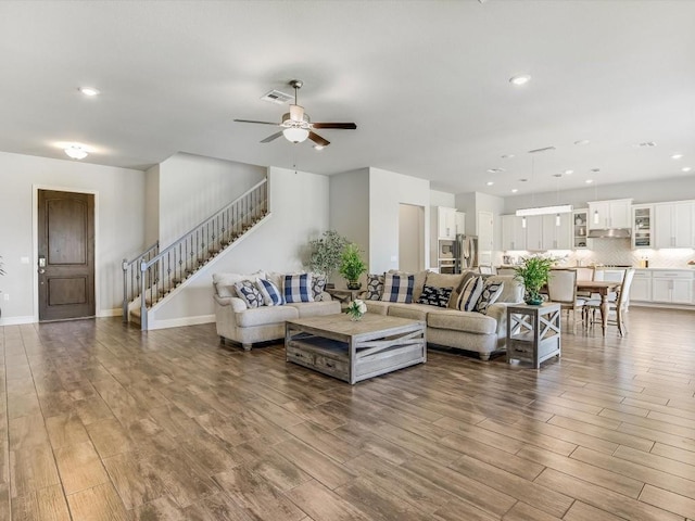 living area with recessed lighting, visible vents, wood finished floors, baseboards, and stairs