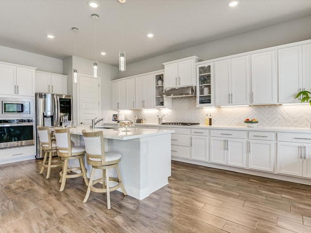 kitchen with a kitchen island with sink, pendant lighting, backsplash, appliances with stainless steel finishes, and white cabinets