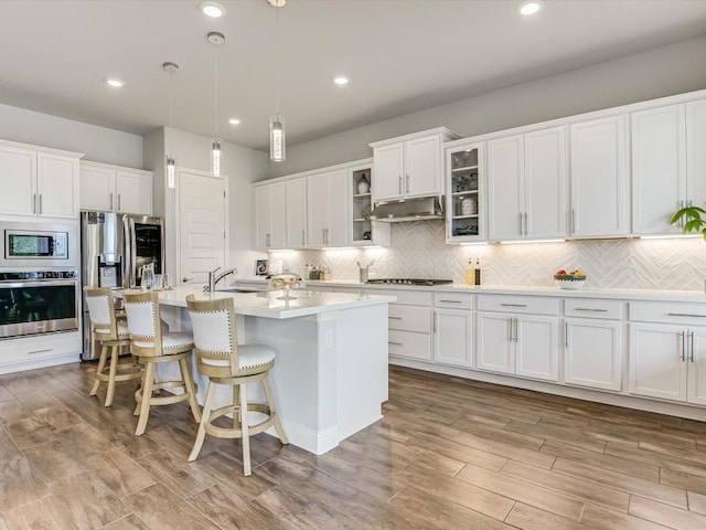 kitchen with stainless steel appliances, backsplash, white cabinetry, and under cabinet range hood
