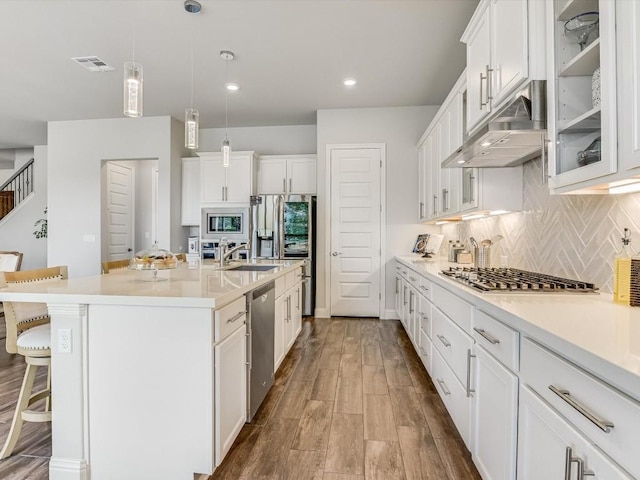 kitchen featuring decorative backsplash, appliances with stainless steel finishes, under cabinet range hood, a kitchen bar, and white cabinetry