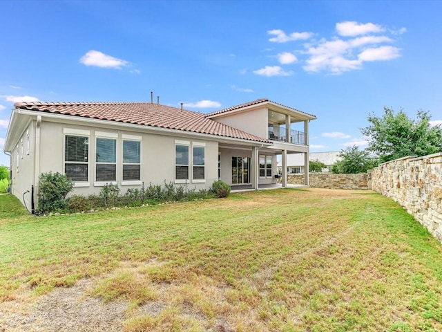 back of property with a lawn, a tile roof, a balcony, and stucco siding