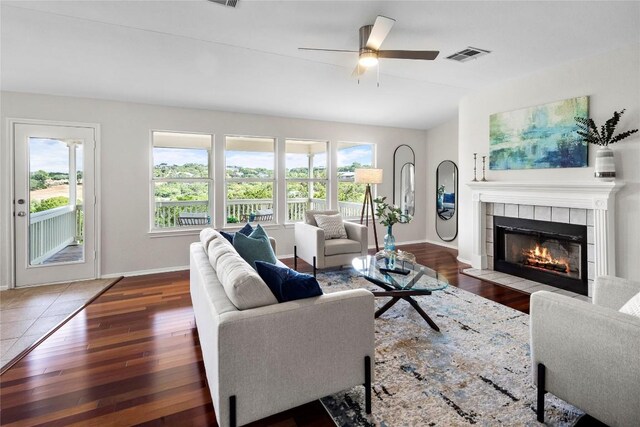 living room with visible vents, a tile fireplace, baseboards, and wood-type flooring