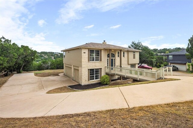 bi-level home with concrete driveway, an attached garage, stone siding, and a chimney