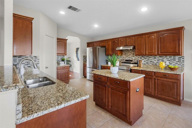 kitchen featuring visible vents, a sink, light stone counters, under cabinet range hood, and appliances with stainless steel finishes