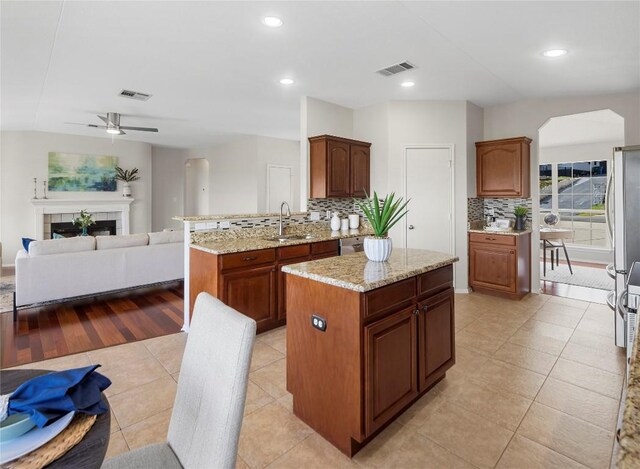 kitchen featuring visible vents, a tile fireplace, open floor plan, backsplash, and a center island