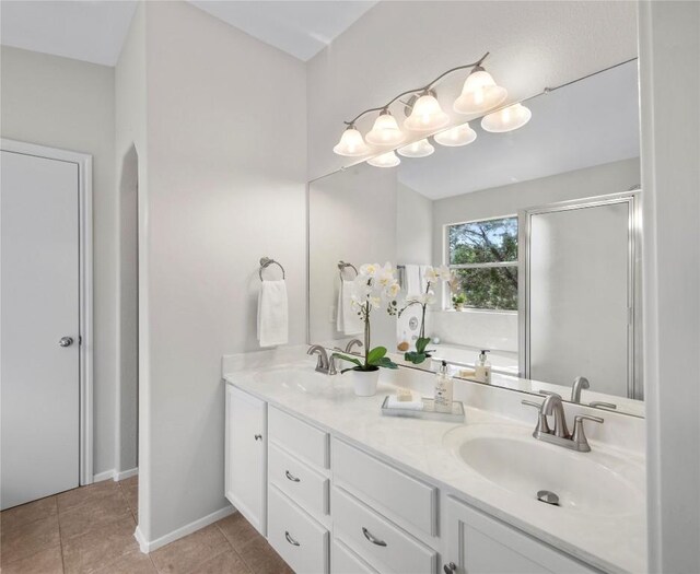 full bath with tile patterned flooring, double vanity, a shower stall, and a sink