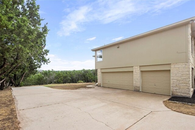 view of side of property featuring stone siding, stucco siding, concrete driveway, and a garage