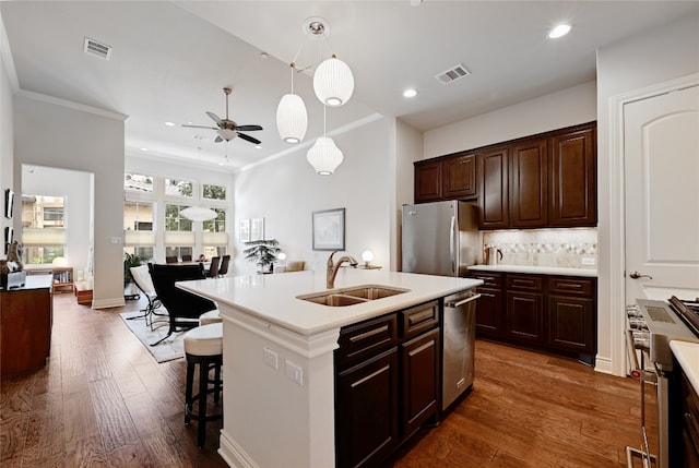 kitchen with appliances with stainless steel finishes, a kitchen island with sink, hanging light fixtures, sink, and ceiling fan