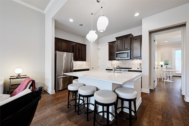 kitchen featuring dark hardwood / wood-style floors, a center island with sink, appliances with stainless steel finishes, tasteful backsplash, and hanging light fixtures