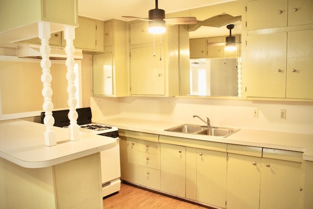 kitchen with light wood-type flooring, white gas range oven, kitchen peninsula, sink, and ceiling fan