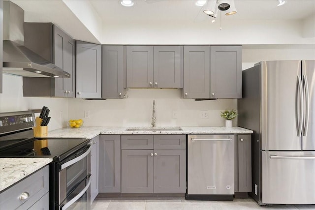 kitchen featuring wall chimney exhaust hood, sink, gray cabinetry, light stone counters, and stainless steel appliances