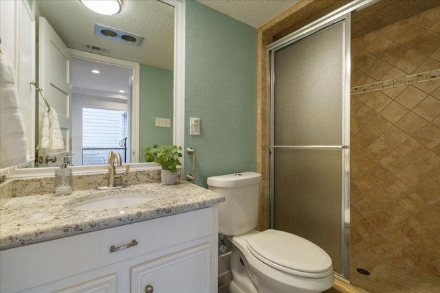 bathroom with vanity, toilet, a shower with shower door, and a textured ceiling