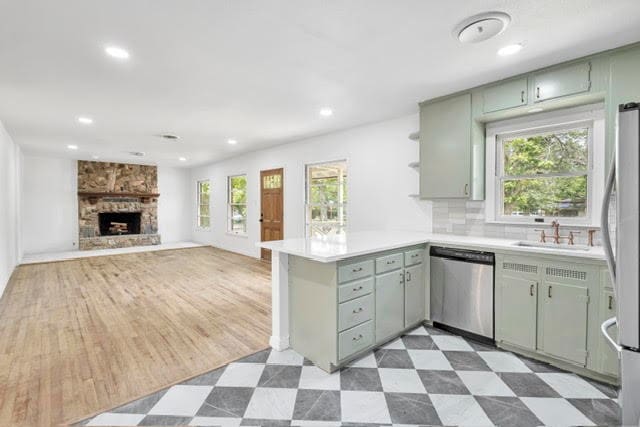 kitchen with sink, stainless steel appliances, green cabinets, a stone fireplace, and kitchen peninsula