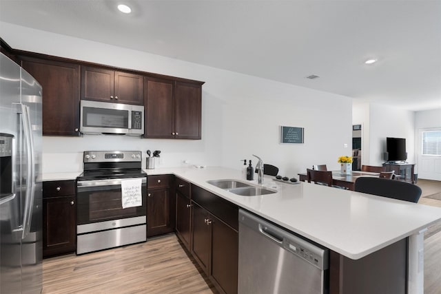 kitchen featuring light hardwood / wood-style floors, a breakfast bar area, sink, kitchen peninsula, and stainless steel appliances