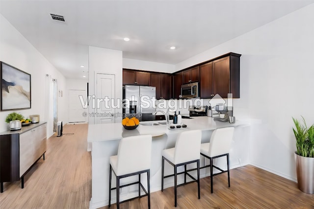 kitchen with a kitchen bar, stainless steel appliances, light hardwood / wood-style floors, and kitchen peninsula