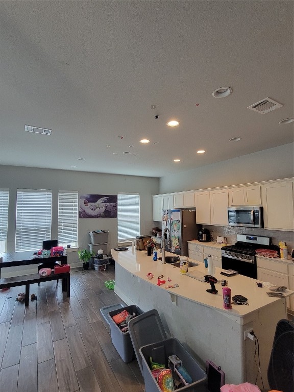 kitchen featuring white cabinets, appliances with stainless steel finishes, a center island with sink, and dark wood-type flooring