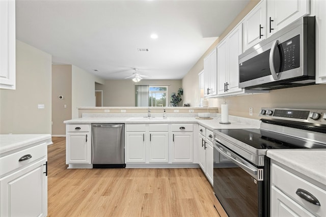 kitchen with light wood finished floors, stainless steel appliances, visible vents, white cabinets, and a sink