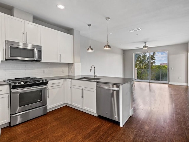kitchen featuring decorative backsplash, appliances with stainless steel finishes, dark countertops, a sink, and a peninsula