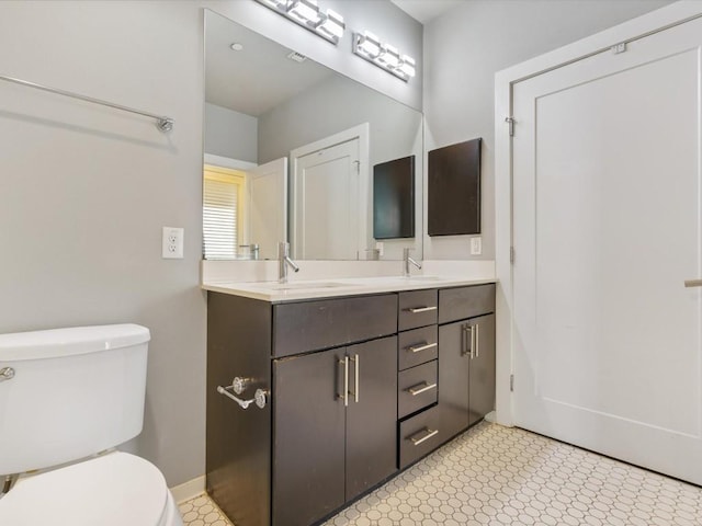 bathroom featuring double vanity, toilet, baseboards, and a sink