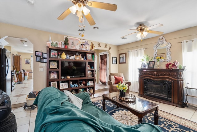 living room featuring light tile patterned floors, a fireplace, arched walkways, and a ceiling fan