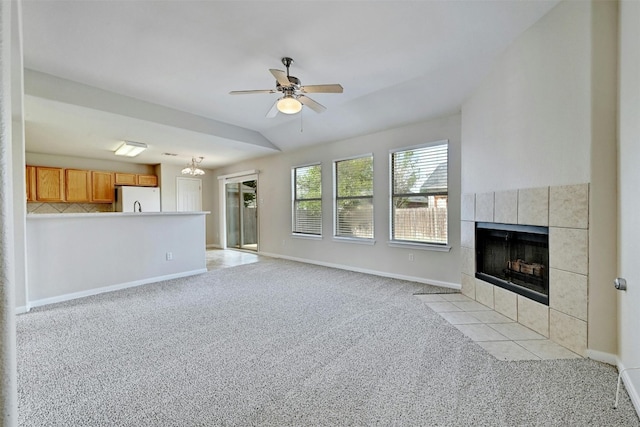 unfurnished living room featuring ceiling fan with notable chandelier, light carpet, and a tiled fireplace