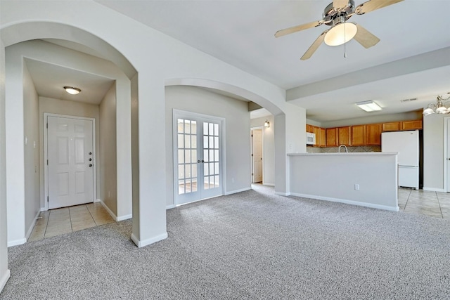 unfurnished living room with ceiling fan with notable chandelier, light colored carpet, and french doors