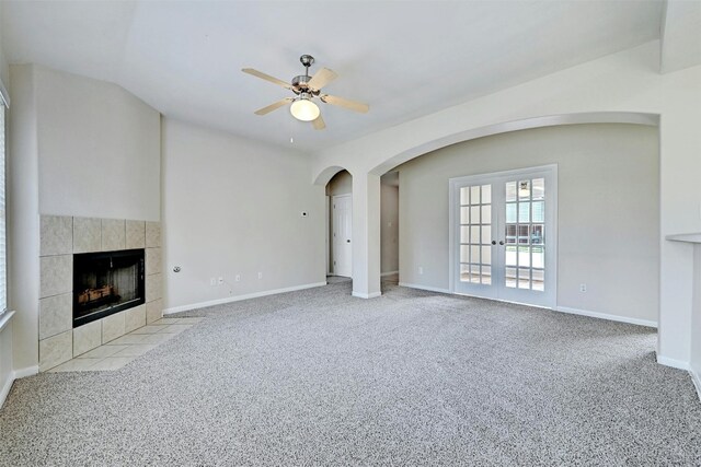 unfurnished living room with french doors, light colored carpet, ceiling fan, and a tiled fireplace