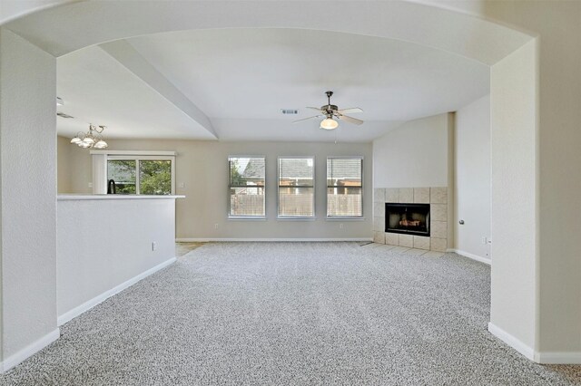 unfurnished living room featuring lofted ceiling, light carpet, a fireplace, and ceiling fan with notable chandelier