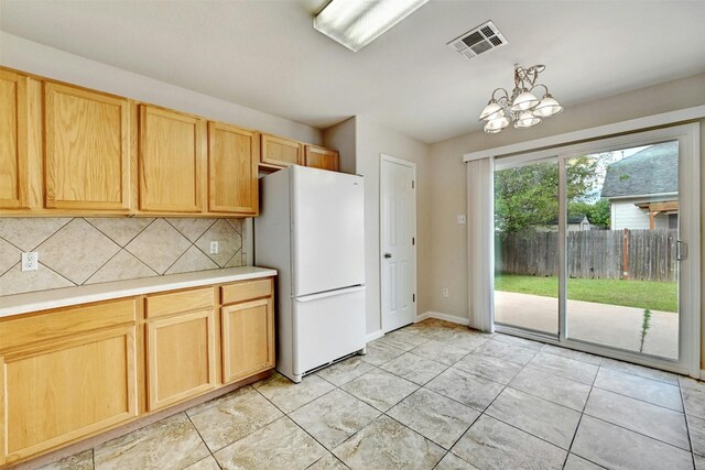 kitchen featuring light brown cabinets, white refrigerator, a chandelier, decorative backsplash, and light tile patterned floors