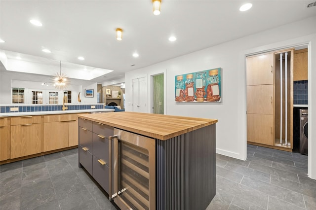 kitchen with butcher block counters, a center island, washer / clothes dryer, beverage cooler, and light brown cabinets